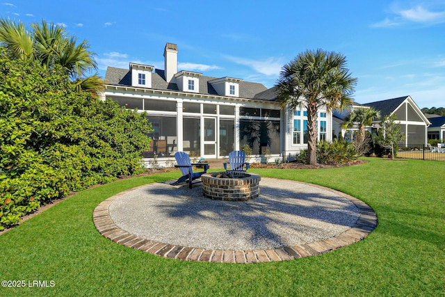 rear view of house featuring an outdoor fire pit, a sunroom, a chimney, a patio area, and a lawn