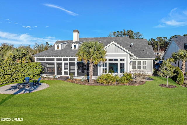 back of property with a lawn, board and batten siding, an outdoor fire pit, and a sunroom