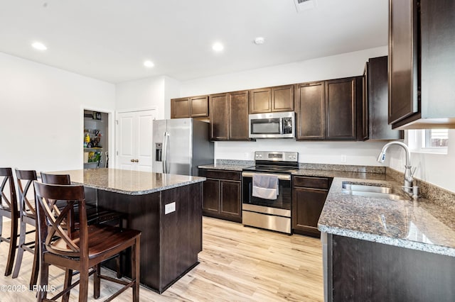 kitchen featuring appliances with stainless steel finishes, dark brown cabinetry, a sink, dark stone countertops, and a kitchen bar