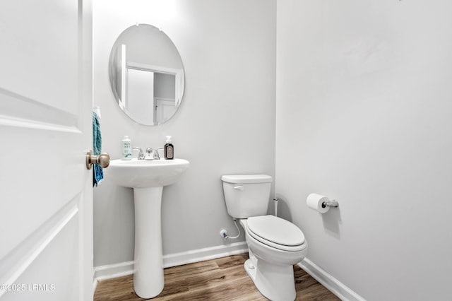 half bathroom with baseboards, toilet, and wood finished floors