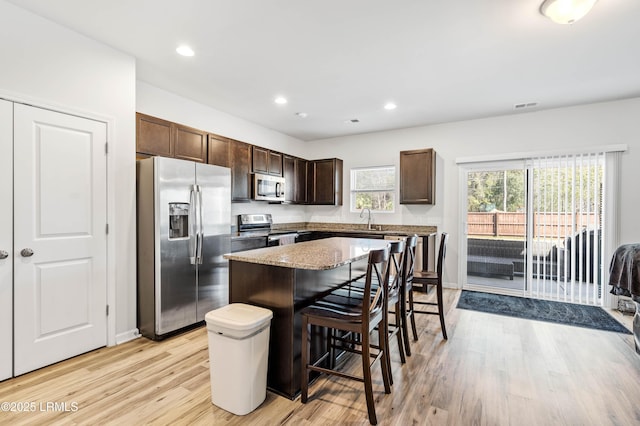 kitchen featuring dark brown cabinetry, a kitchen island, appliances with stainless steel finishes, a breakfast bar, and light wood-type flooring