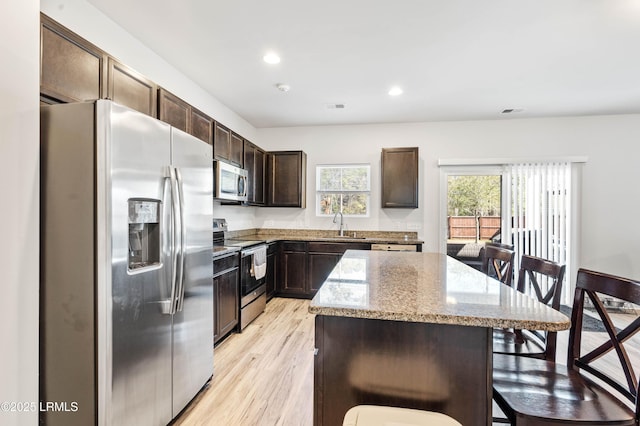 kitchen featuring a kitchen island, a kitchen breakfast bar, dark brown cabinets, appliances with stainless steel finishes, and light stone countertops