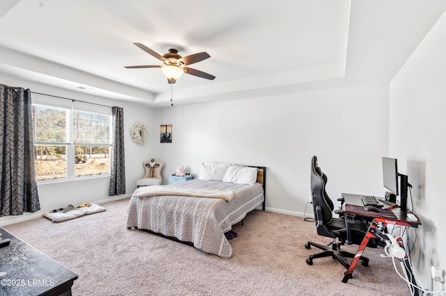 carpeted bedroom featuring a ceiling fan, a tray ceiling, and baseboards