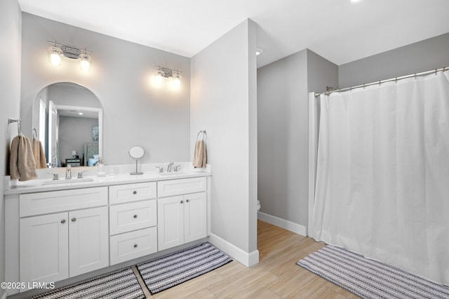 bathroom with toilet, a sink, baseboards, and double vanity