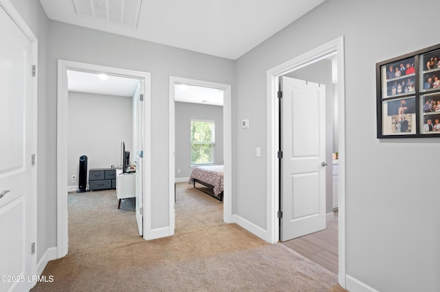 hallway with visible vents, light carpet, and baseboards