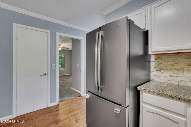 kitchen featuring stainless steel refrigerator, white cabinetry, backsplash, light stone counters, and crown molding