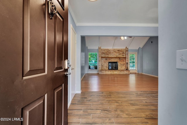 unfurnished living room featuring hardwood / wood-style flooring, ornamental molding, vaulted ceiling, and a brick fireplace