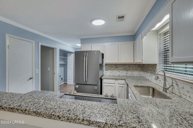 kitchen with sink, white cabinetry, light stone counters, stainless steel fridge, and decorative backsplash