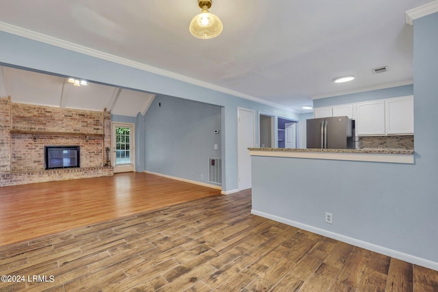 unfurnished living room featuring crown molding, a fireplace, vaulted ceiling, and light wood-type flooring