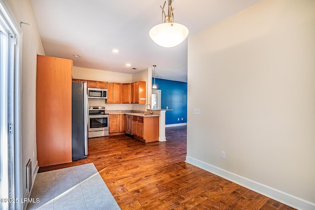 kitchen featuring sink, hanging light fixtures, appliances with stainless steel finishes, dark hardwood / wood-style floors, and kitchen peninsula