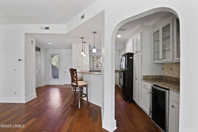 kitchen featuring wine cooler, freestanding refrigerator, glass insert cabinets, dark stone countertops, and a breakfast bar