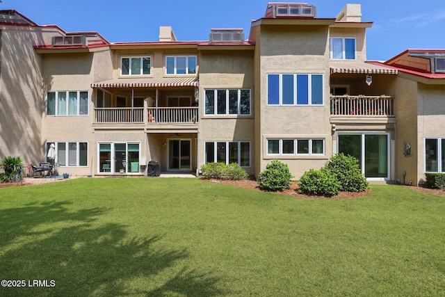 back of house featuring a balcony, stucco siding, central AC unit, and a yard