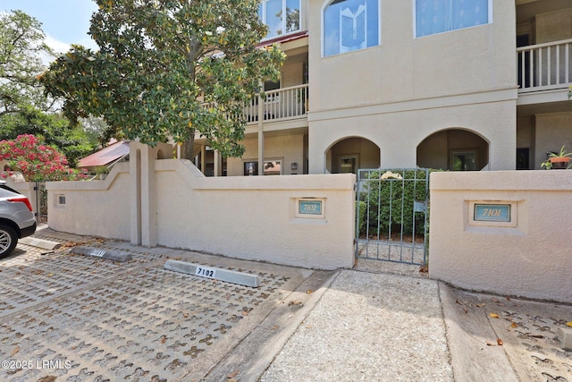 view of side of home featuring a fenced front yard, stucco siding, a gate, uncovered parking, and a balcony