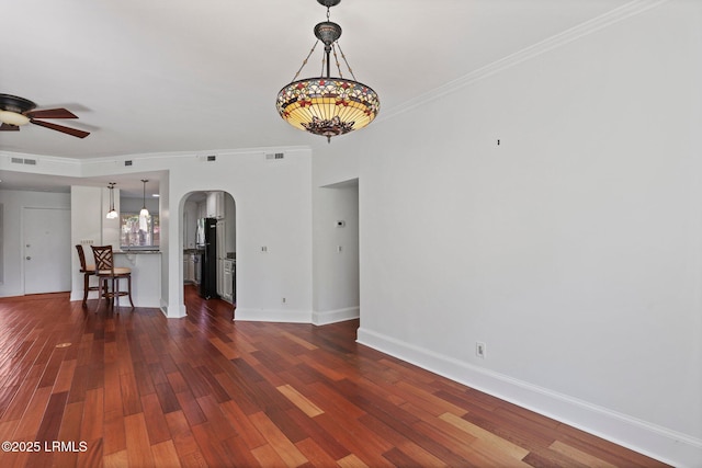 unfurnished living room with arched walkways, ceiling fan, baseboards, dark wood finished floors, and ornamental molding