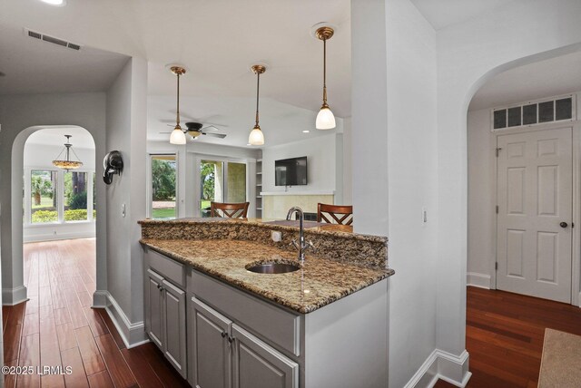 kitchen with arched walkways, a sink, baseboards, dark wood-type flooring, and light stone countertops