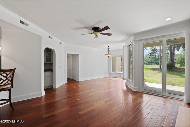 unfurnished living room featuring a ceiling fan, arched walkways, baseboards, wood finished floors, and ornamental molding