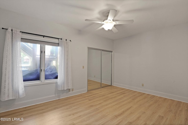unfurnished bedroom with light wood-type flooring, a closet, baseboards, and a ceiling fan