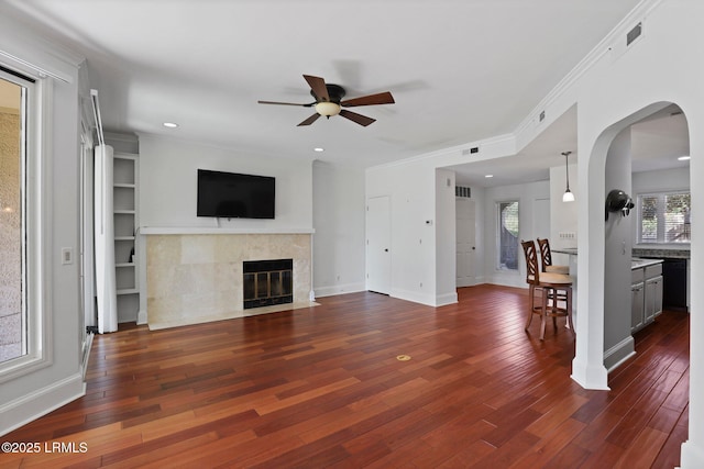 unfurnished living room with a ceiling fan, a tiled fireplace, dark wood finished floors, baseboards, and recessed lighting
