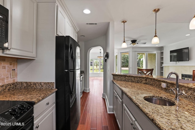 kitchen with black appliances, backsplash, arched walkways, stone countertops, and a ceiling fan