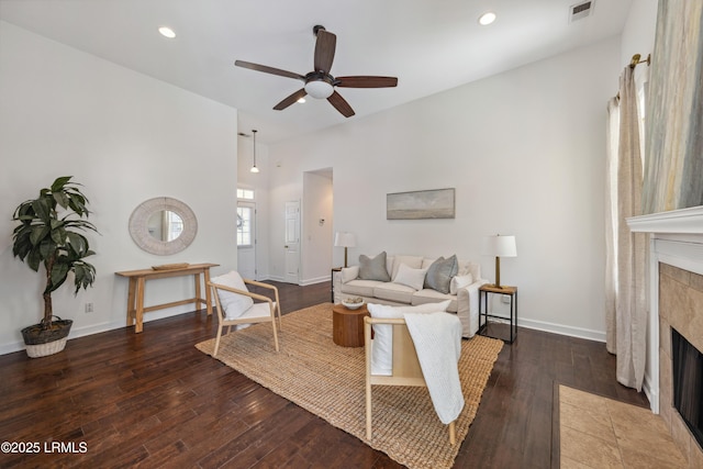 living room with a tiled fireplace, a ceiling fan, visible vents, and wood-type flooring