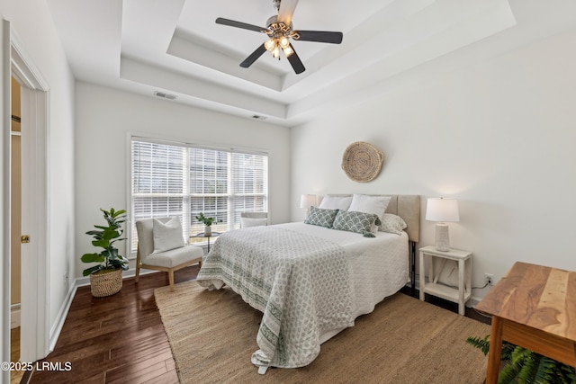 bedroom with visible vents, a tray ceiling, wood finished floors, baseboards, and ceiling fan