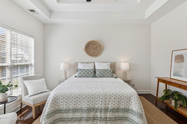 bedroom with visible vents, baseboards, a tray ceiling, and wood finished floors