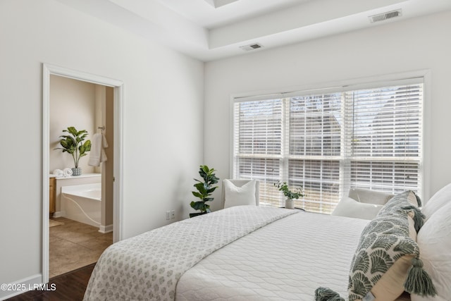 bedroom featuring visible vents, connected bathroom, baseboards, and wood finished floors