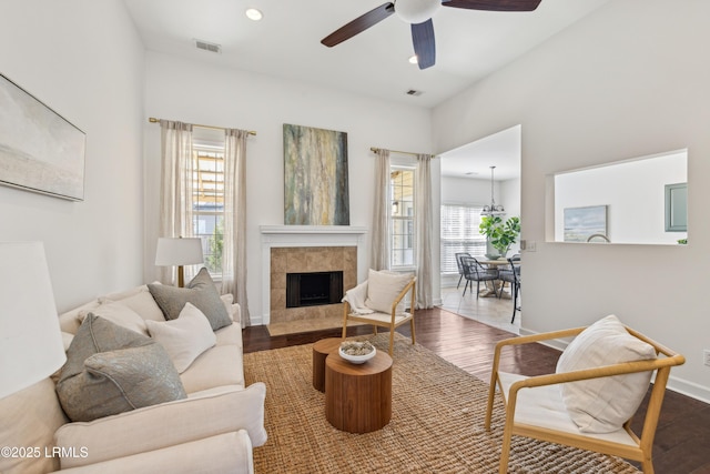 living room featuring a tile fireplace, wood finished floors, visible vents, and ceiling fan