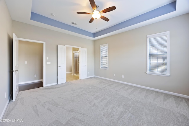 unfurnished bedroom with ensuite bath, light colored carpet, ceiling fan, and a tray ceiling