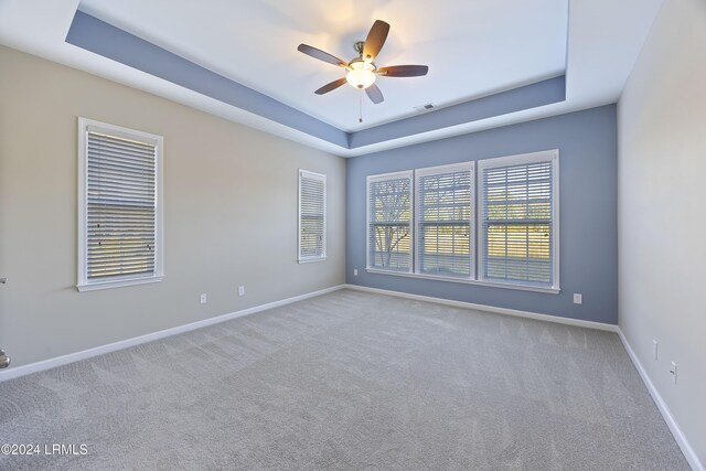 spare room with ceiling fan, a tray ceiling, and light carpet