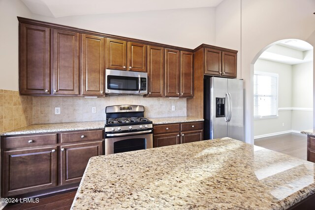 kitchen featuring appliances with stainless steel finishes, dark hardwood / wood-style floors, backsplash, and light stone counters