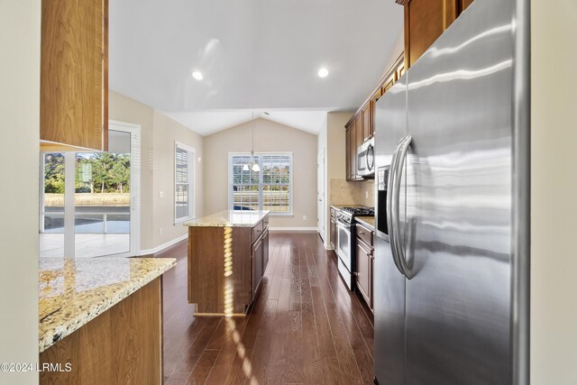 kitchen featuring appliances with stainless steel finishes, lofted ceiling, backsplash, a center island, and light stone counters