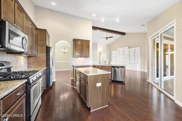 kitchen with a kitchen island, appliances with stainless steel finishes, kitchen peninsula, light stone countertops, and dark wood-type flooring