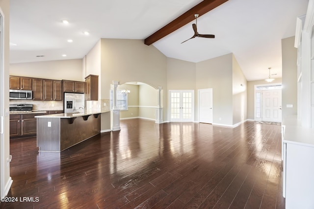 kitchen with dark wood-type flooring, beam ceiling, stainless steel appliances, tasteful backsplash, and a kitchen bar