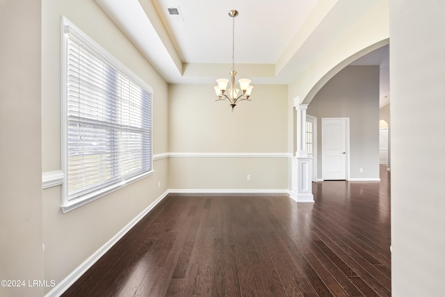 spare room with ornate columns, dark hardwood / wood-style floors, a notable chandelier, and a tray ceiling