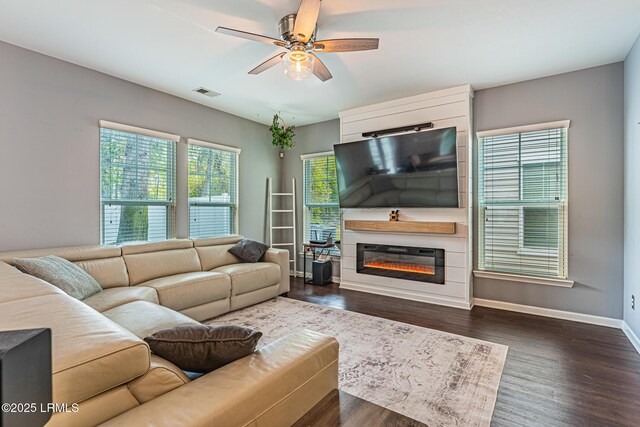 living area featuring ceiling fan, visible vents, baseboards, dark wood-style floors, and a glass covered fireplace
