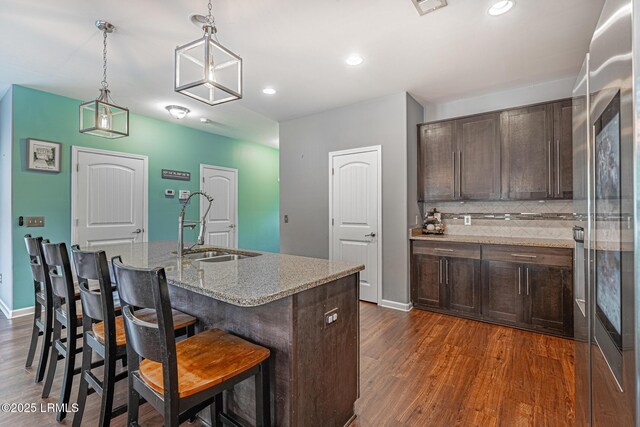 kitchen featuring dark brown cabinetry, a breakfast bar, light stone counters, a sink, and dark wood finished floors