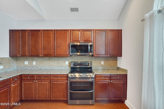 kitchen featuring vaulted ceiling, light wood-type flooring, appliances with stainless steel finishes, light stone countertops, and decorative backsplash