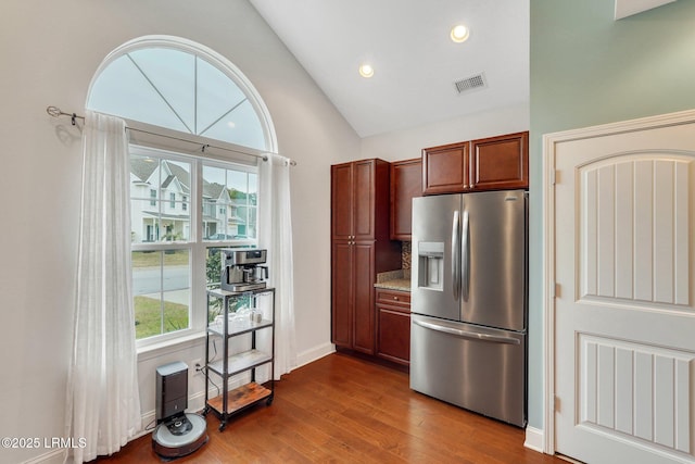 kitchen with stainless steel refrigerator with ice dispenser, vaulted ceiling, light stone counters, and hardwood / wood-style flooring