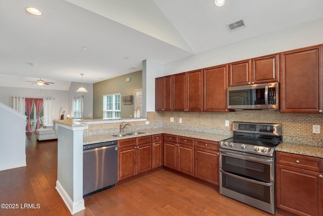 kitchen featuring vaulted ceiling, decorative light fixtures, sink, kitchen peninsula, and stainless steel appliances