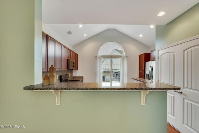 kitchen featuring vaulted ceiling, appliances with stainless steel finishes, a kitchen bar, dark stone counters, and kitchen peninsula