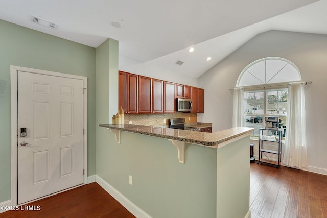 kitchen with lofted ceiling, a kitchen bar, dark stone countertops, appliances with stainless steel finishes, and decorative backsplash