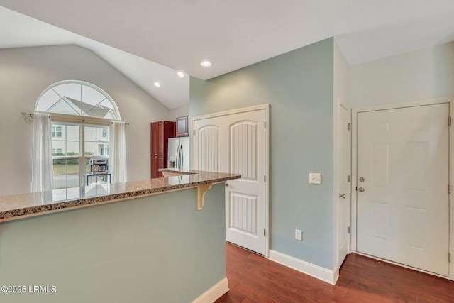 kitchen featuring stainless steel refrigerator with ice dispenser, lofted ceiling, a kitchen bar, dark hardwood / wood-style flooring, and light stone countertops