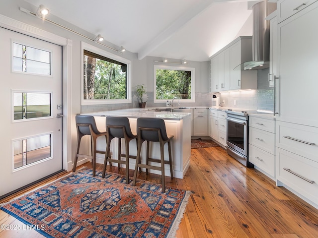 2065 Deer Island Rd, Hilton Head Island, SC 29928 - kitchen featuring stainless steel range with electric stovetop, a kitchen breakfast bar, wall chimney range hood, decorative backsplash, and light wood-style floors