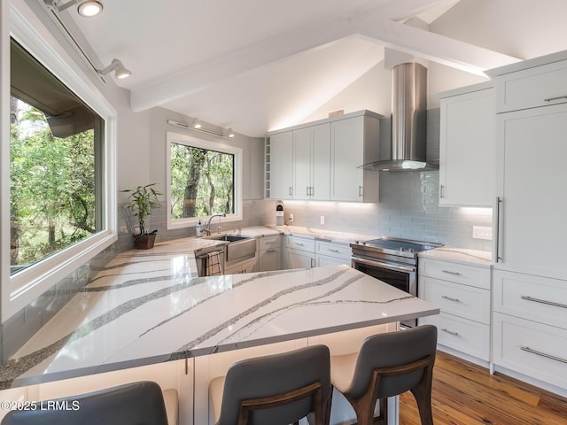 2065 Deer Island Rd, Hilton Head Island, SC 29928 - kitchen with wall chimney exhaust hood, light stone countertops, a breakfast bar area, decorative backsplash, and a peninsula