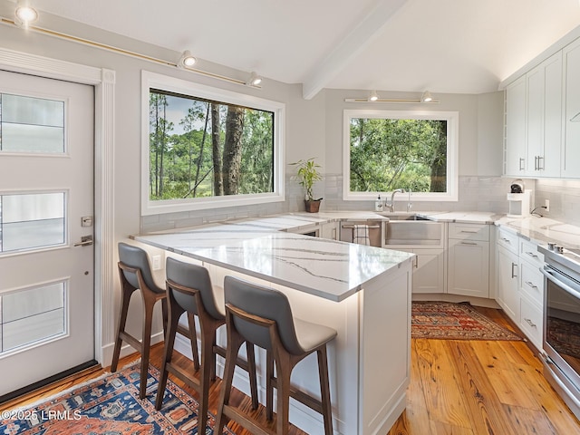 2065 Deer Island Rd, Hilton Head Island, SC 29928 - kitchen with light stone counters, a breakfast bar, light wood-style floors, tasteful backsplash, and white cabinets