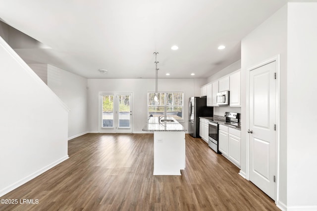 kitchen with stainless steel appliances, an island with sink, hanging light fixtures, and white cabinets