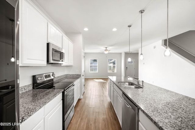 kitchen featuring stainless steel appliances, light wood-style floors, a ceiling fan, white cabinetry, and a sink