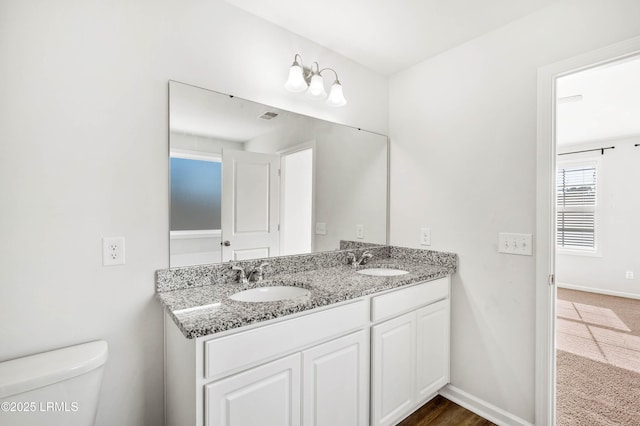 bathroom with baseboards, a sink, toilet, and double vanity