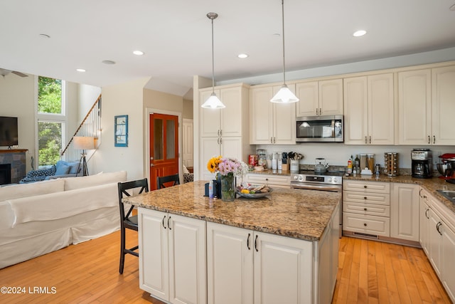 kitchen with a breakfast bar, decorative light fixtures, a center island, light wood-type flooring, and appliances with stainless steel finishes